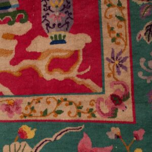 Close-up of an ornate rug featuring a magenta field, a gray vase motif, and a wide floral border on teal green.