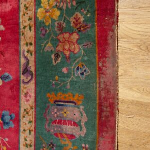 Worn pink, teal, and tan rug with dense floral and vase patterns rests against wood plank flooring.