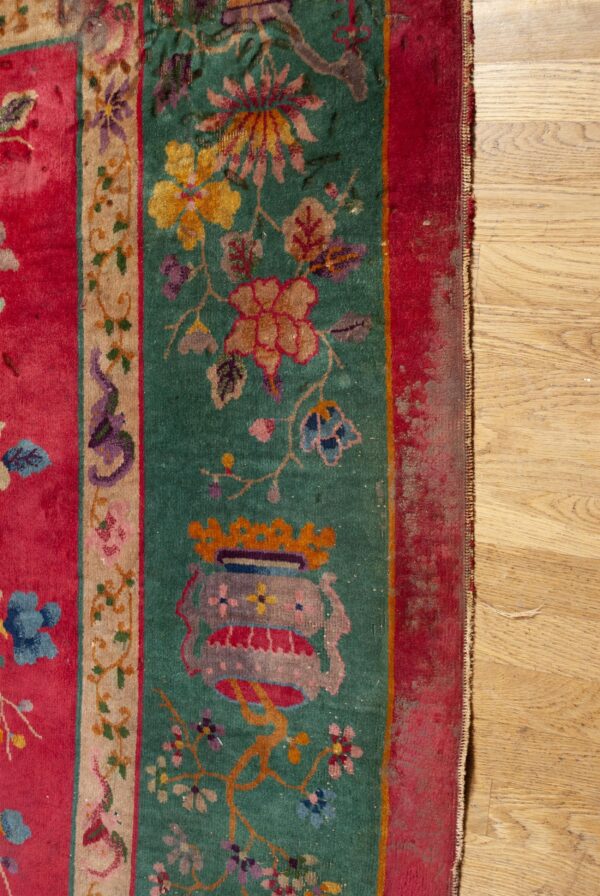 Worn pink, teal, and tan rug with dense floral and vase patterns rests against wood plank flooring.