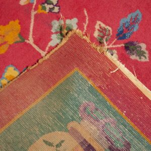 Bright pink high-pile rug with colorful floral motifs is folded back revealing the woven teal and red backing.