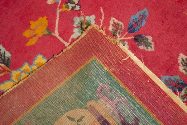 Bright pink high-pile rug with colorful floral motifs is folded back revealing the woven teal and red backing.