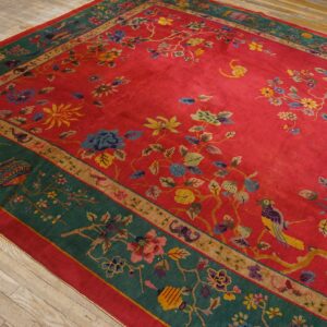 Red field rug with multicolored floral vine and bird patterns and a wide green border on hardwood.