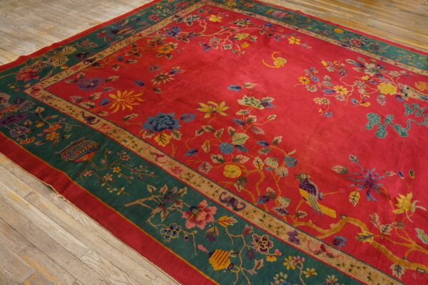 Red field rug with multicolored floral vine and bird patterns and a wide green border on hardwood.