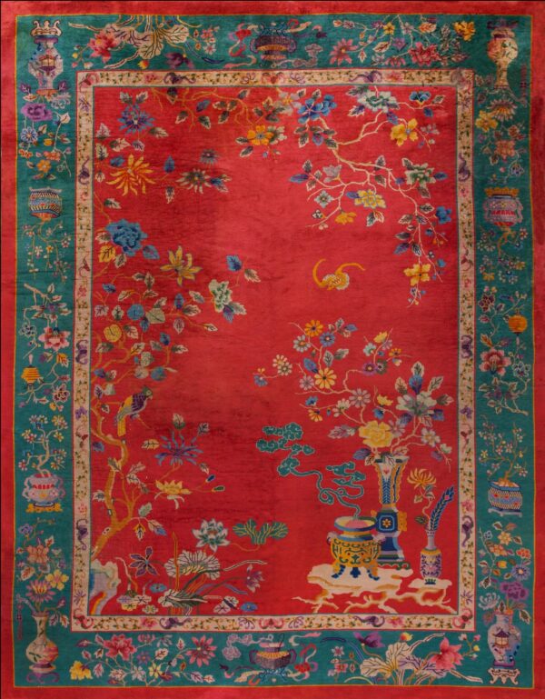 Ornate red rug with a wide teal border filled with elaborate multi-color botanical and vase designs.