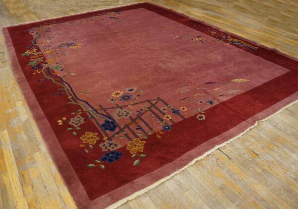 Plush mauve rug with a maroon border and scattered multicolored flowers on worn wooden floorboards.