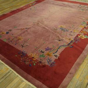 A large dusty pink rug with a deep red border features scattered multicolor floral patterns on wood flooring.