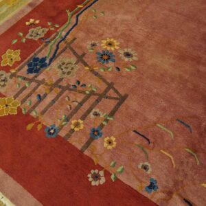 Dusty rose rug with deep red border and colorful floral trellis pattern rests on wood planks.