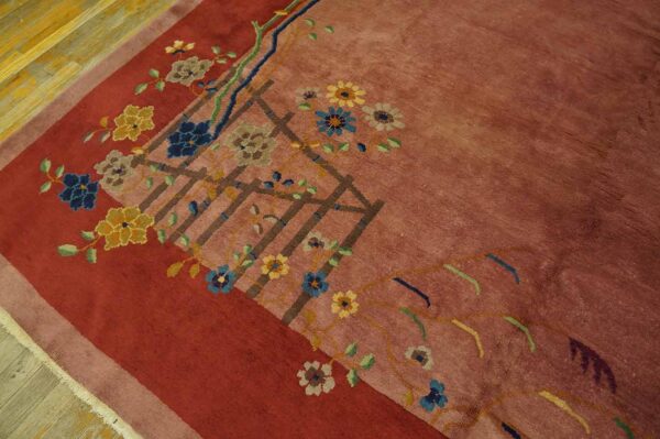 Dusty rose rug with deep red border and colorful floral trellis pattern rests on wood planks.