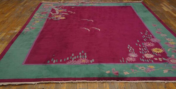 Deep pink rug featuring a teal border, stylized floral sprays, and two flying birds on wood flooring.
