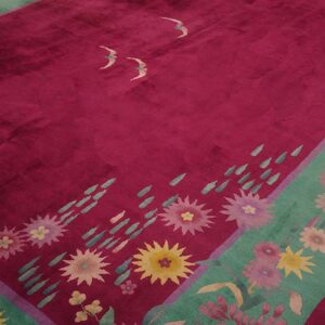 Magenta pile rug with a green floral border and stylized bird motifs resting on wood flooring.