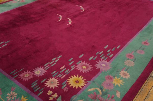Magenta pile rug with a green floral border and stylized bird motifs resting on wood flooring.