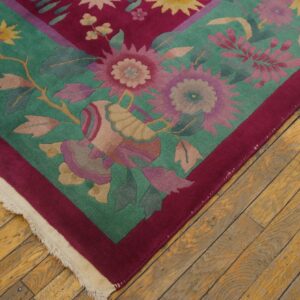 Teal and magenta floral rug corner with fringe lies on rustic wood flooring.
