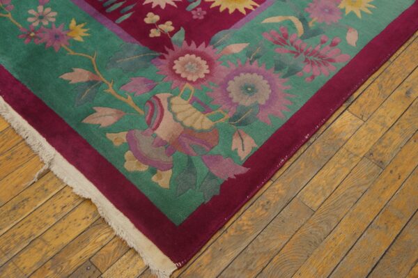 Teal and magenta floral rug corner with fringe lies on rustic wood flooring.