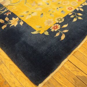 Navy blue border and yellow field rug with floral pattern rests on golden hardwood flooring.