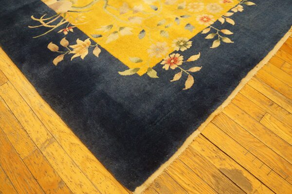 Navy blue border and yellow field rug with floral pattern rests on golden hardwood flooring.