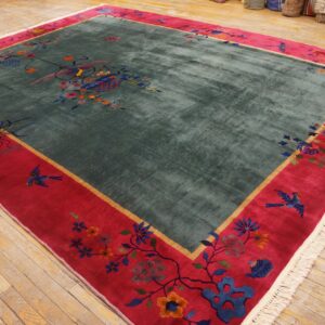 Teal pile rug with deep red border, featuring colorful birds and floral designs on wood floors.