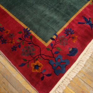 High-pile rug corner showing a green field, red floral border, cream fringe, and distressed wood floor.