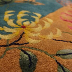 Dense pile rug detail featuring yellow, pink, and green floral designs against teal and camel-colored sections.