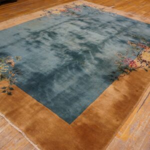 Plush teal rug with a golden tan border and corner floral patterns on distressed wood flooring.