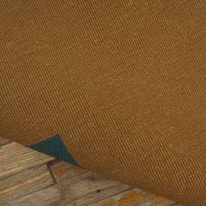 The ribbed brown rug backing is lifted, showing a dark green layer and distressed wood planks below.