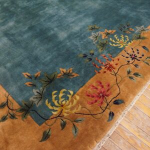 Close-up of a teal rug corner with a golden border and colorful floral patterns on wood flooring.