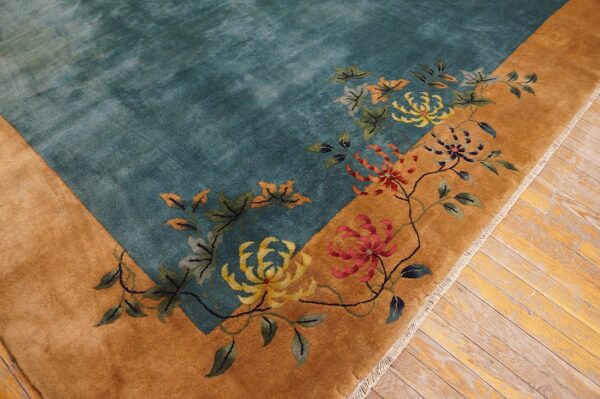 Close-up of a teal rug corner with a golden border and colorful floral patterns on wood flooring.