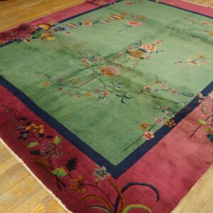 Square rug featuring a seafoam green field with floral motifs and a wide magenta border on wood floors.