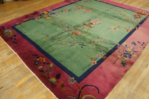 Square rug featuring a seafoam green field with floral motifs and a wide magenta border on wood floors.