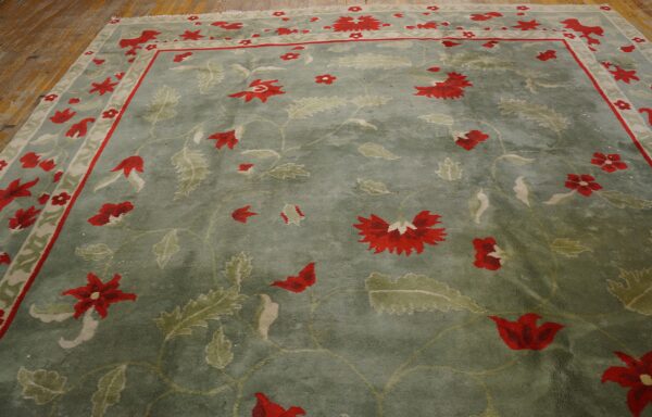Green floral rug with bright red flowers and leafy motifs visible on hardwood planks.