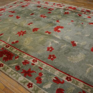 Distressed sage green rug with scattered red floral patterns and a border lies on rustic wood flooring.