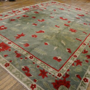 Large sage green rug features a red and light green floral border on distressed plank flooring.