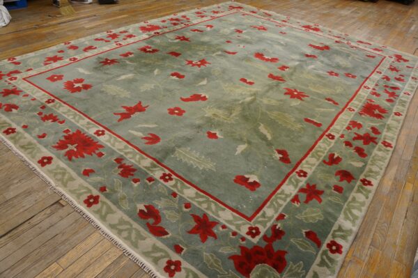 Large sage green rug features a red and light green floral border on distressed plank flooring.