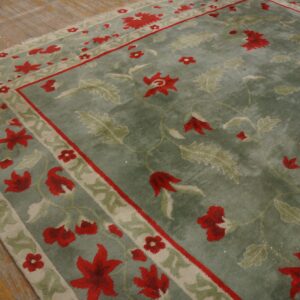 A sage green rug with red and pale green floral patterns lies on distressed hardwood flooring.