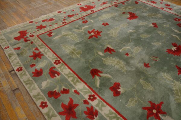 A sage green rug with red and pale green floral patterns lies on distressed hardwood flooring.