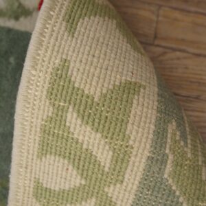 A rolled rug shows its tight beige and sage woven back, with glimpses of red pile above wood flooring.