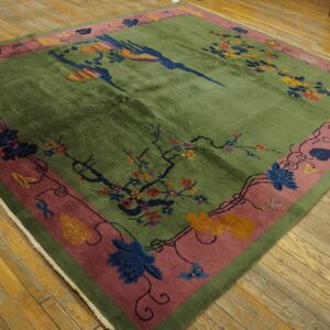 Square green rug with colorful birds and floral vines, wide rose border, displayed on distressed wood floors.