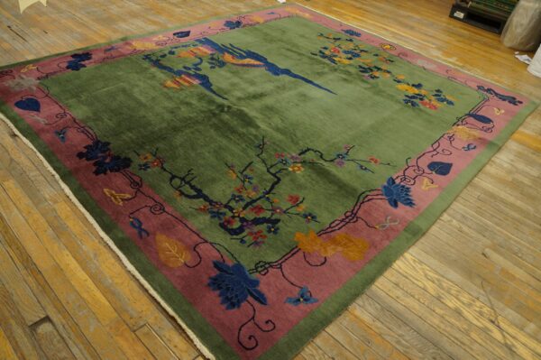 Square green rug with colorful birds and floral vines, wide rose border, displayed on distressed wood floors.