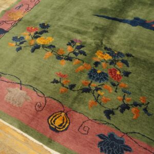 Olive green rug with high pile, colorful floral vines, wide mauve border, lying on wood planks.