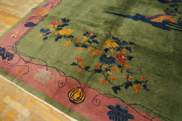 Olive green rug with high pile, colorful floral vines, wide mauve border, lying on wood planks.