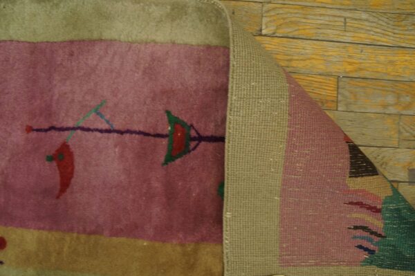 Pink rug with a stylized red pepper and arrow design is curled back, showing woven backing on wood floor.
