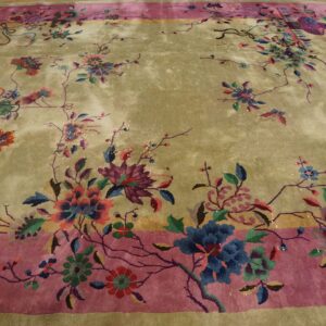 Greenish-gold rug with a rose border and vibrant blue, pink, and purple floral motifs on a wood floor.