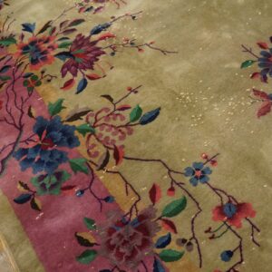 Multicolor floral pattern on a sage green rug with a pink stripe, visible on distressed wood flooring.