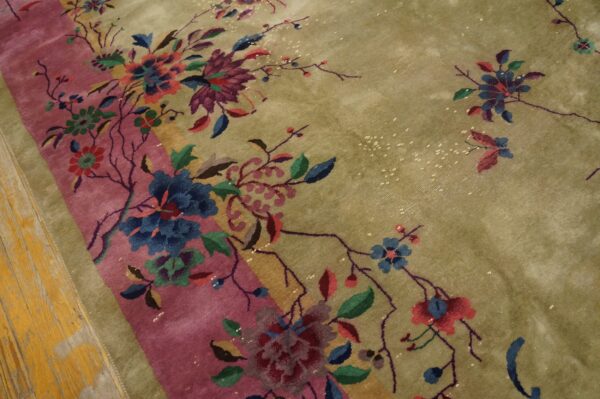 Multicolor floral pattern on a sage green rug with a pink stripe, visible on distressed wood flooring.