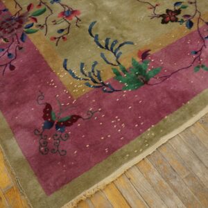 Corner of an olive green and magenta rug with colorful floral and butterfly patterns on wood planks.