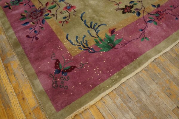 Corner of an olive green and magenta rug with colorful floral and butterfly patterns on wood planks.