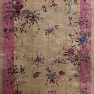 A beige rug with a wide pink border features colorful stylized floral branches and detailed decorative motifs.
