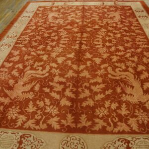 Ornate rust-colored rug with beige border and symmetrical bird pattern displayed on distressed wood planks.