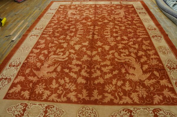 Ornate rust-colored rug with beige border and symmetrical bird pattern displayed on distressed wood planks.