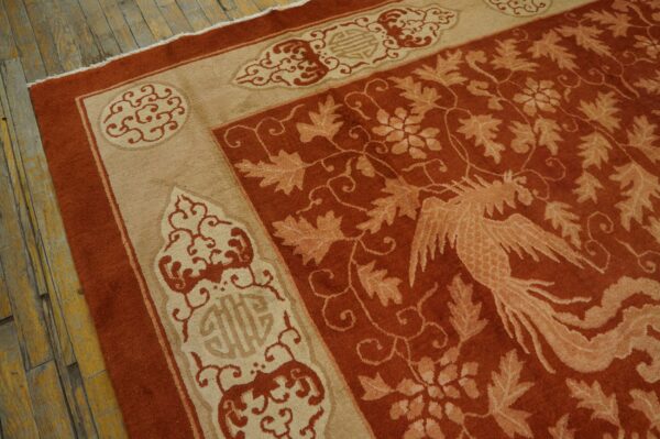Terracotta and tan rug with a phoenix and leaf pattern borders worn wooden floorboards.