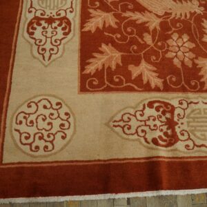 Rust and tan rug detail showing ornate scrollwork, botanical patterns, and a thick border on wooden planks.